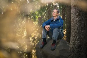 FinFamin Labyrintti-lehdessä 3/2021 mielenterveysomainen Samu Moilanen istuu kuvassa kivellä metsässä _Kuva Petra Tiihonen